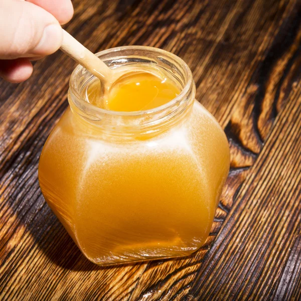 Borcan de miere și lingură pe un fundal din lemn — Fotografie, imagine de stoc