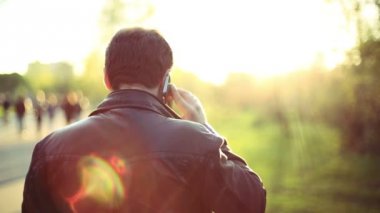 Adam cep telefonu üzerinde günbatımında parkta arıyor. Arkadan görüntüleyin. Smartphone üzerinde konuşan adam. HD 1080.