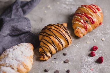 Tahta üzerinde üç taze kruvasan ve gri peçete.