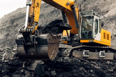 Kazıcı ağır bir maden kamyonunun arkasına kömür yüklüyor. Kömür madenciliğini aç.