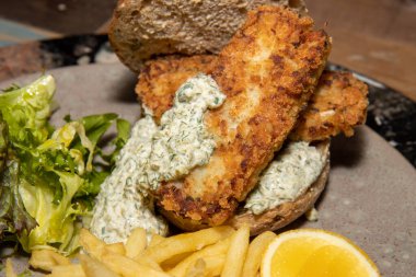 Ahşap mutfak masasında füme mezgit balığı, patates kızartması ve Tatar soslu sandviç.