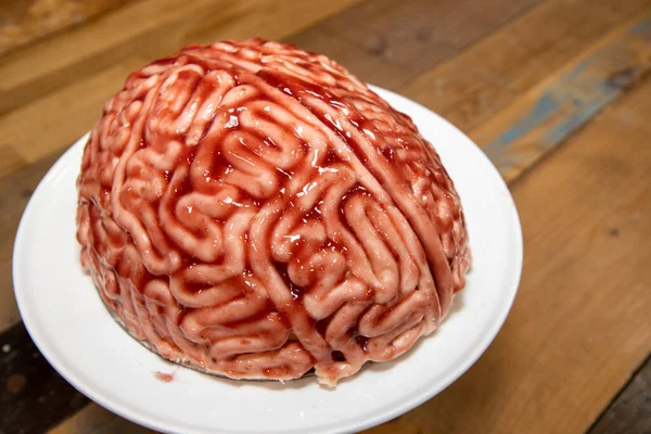 A cake in the shape of a brain with strawberry source brushed on it to make the sponge cake look like a real human bloody brain for the halloween party food desert