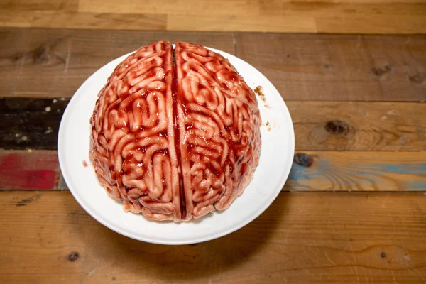 A cake in the shape of a brain with strawberry source brushed on it to make the sponge cake look like a real human bloody brain for the halloween party food desert