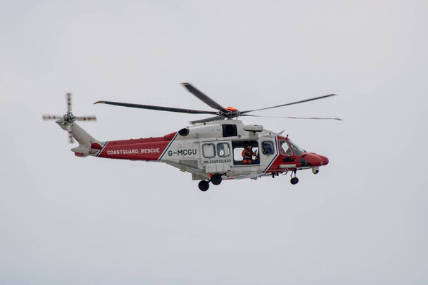 East Sussex, Beachy Head, UK 10th July 2019: The HM Coastguard Rescue Helicopter attending an incident on the Beachy Head cliffs flying in the sky on a bright cloudy day over the ocean.