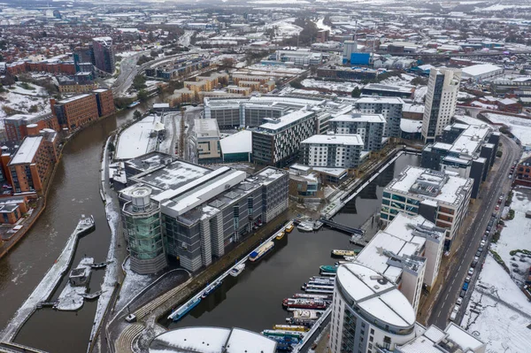 Aerial photo of a snowy winters day in the city of Leeds in the UK showing the area in Leeds known as the Leeds Dock near the Leeds and Liverpool canal and the Royal Armouries Museum covered in snow.