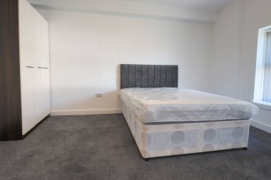 Yeni dekore edilmiş tipik bir İngiliz yatak odası. Geniş yatağı, beyaz duvarları ve gri halısı var.