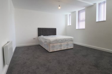 Yeni dekore edilmiş tipik bir İngiliz yatak odası. Geniş yataklı, beyaz duvarlı, camları perdeli gri bir halı..