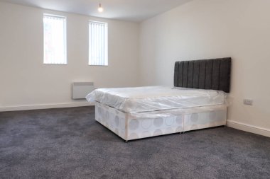 Yeni dekore edilmiş tipik bir İngiliz yatak odası. Geniş yataklı, beyaz duvarlı, camları perdeli gri bir halı..