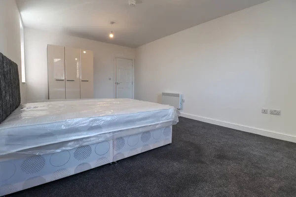 A newly decorated typical British UK bedroom with a large bed, with white walls, grey carpet