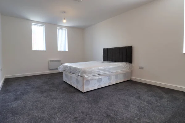 A newly decorated typical British UK bedroom with a large bed and wardrobe, with white walls, grey carpet with blinds at the window.
