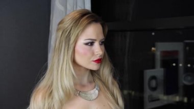 Uzun sarı saçlı, zarif ve çekici bir kadın. Canı sıkkın görünüyor. Dairesinin penceresinden dışarı bakıyor..