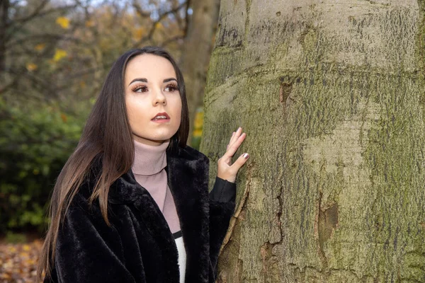 黒いコートを着た森の公園で冬の時間に長い茶色の髪の若い魅力的な女性 — ストック写真