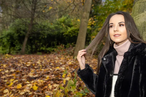 黒いコートを着た森の公園で冬の時間に長い茶色の髪の若い魅力的な女性 — ストック写真