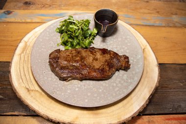 Bir tabak kırmızı şarap soslu ve ahşap mutfak masasında garnitürlü leziz bir fileto biftek.