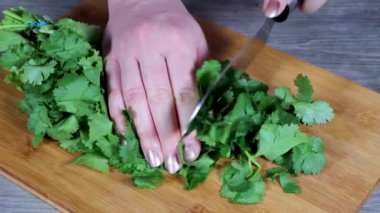 Mutfakta bir kadın odun kesme tahtasına otlar ve kişniş kesiyor, ev yemeği kavramı.