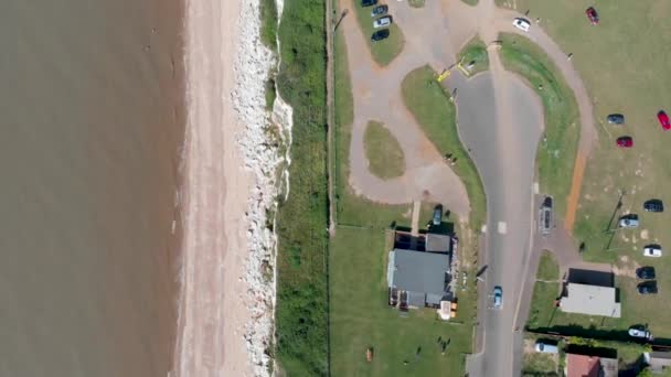 ハンストンノーフォークの英国の海辺の町の空中映像は 崖の上の駐車場と人々がビーチで日光浴と海岸線のビーチと海のトップダウンビューを示しています — ストック動画