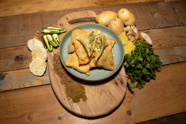 Lezzetli samosaların yapımında kullanılan malzemelerle çevrili ahşap mutfak masasında bulunan lezzetli bir Hint samosası yığını..