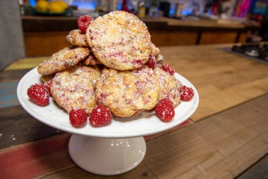 Mutfak masasında taze pişmiş ahududu ve beyaz çikolatalı kurabiyeler sergileniyor.