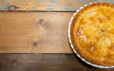 Lezzetli etli bir etli turta, yukarıdan bakınca ahşap mutfak masasının üzerindeki lezzetli etli turtayı ve kabuğu gösteriyor.