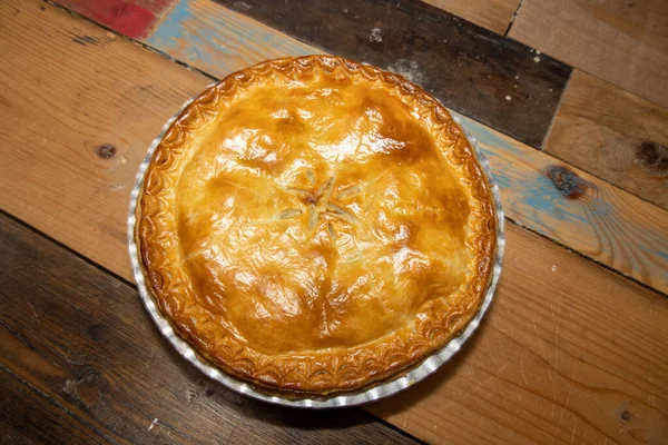 Lezzetli etli bir etli turta, yukarıdan bakınca ahşap mutfak masasının üzerindeki lezzetli etli turtayı ve kabuğu gösteriyor.