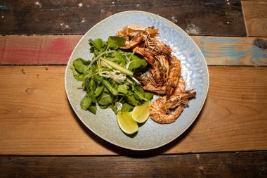 Ahşap mutfak masasında lezzetli bir tabak tuzlu ve biberli karides ve yeşil salata.