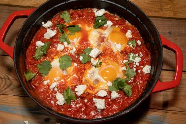 Avokado ve harissa yumurtaları ile büyük kırmızı bir tencerede kaynatılmış lezzetli bir Shakshuka tenceresi.