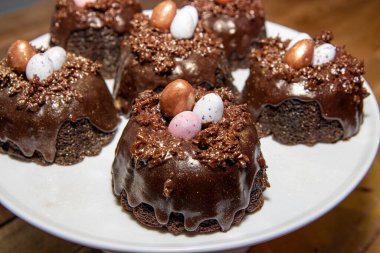 Beyaz bir tabakta üç küçük çikolatalı mini yumurta ile kaplı Paskalya çikolatalı kek seçimi.
