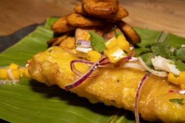 Muz yaprağında servis edilen kızarmış muz dilimleri ile birlikte Batı Afrika 'dan esinlenilmiş lezzetli bir balık ve patates kızartması.