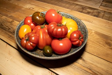 Ahşap mutfak masasında farklı boyutlarda ve renkli domatesler.