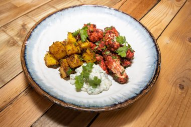 Ahşap mutfak masasında bir tabak lezzetli Tandır Tavuğu ve kimyon tava kızarmış patates.