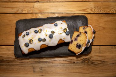 Beyaz kremalı, yaban mersinli ve altın yapraklı ahşap mutfak masasında lezzetli bir yaban mersinli ve limonlu kek.