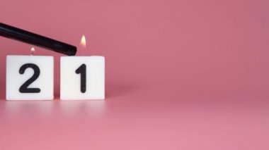 21 numaranın bir doğum gününü veya yıldönümünü kutlayan pembe bir arka planda yanıp söndüğünü söyleyen kare bir mum.