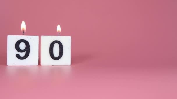 誕生日や記念日を祝うピンクの背景に90番が点灯し 吹き飛ばされているという正方形のろうそく — ストック動画