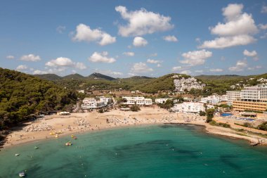 İspanya 'nın İbiza adasının havadan çekilmiş fotoğrafı, İspanya' nın Balear Adaları 'nda yaz mevsiminde Cala Llonga' da güzel plajlar, oteller ve insanları gösteriyor.