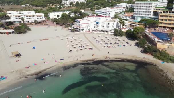 美しいビーチフロントとホテルを示すイビザのスペインの島の航空映像や スペインのバレアレス諸島の夏時間のCala Llongaのビーチの人々 — ストック動画