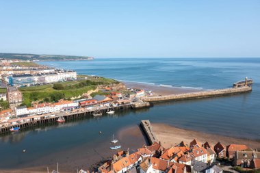 İngiltere 'nin kuzeyindeki Yorkshire kentindeki Whitby kasabasının hava aracı fotoğrafı yazları güneşli bir günde Whitby Jetty ve deniz fenerinin okyanusa açıldığını gösteriyor.