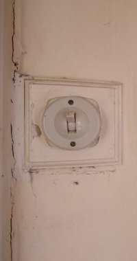 Portrait vertical footage of an old fashioned 1940's British house light switch made out of plastic showing a mans hand turning on and off again the electrical vintage switch in an old bedroom.