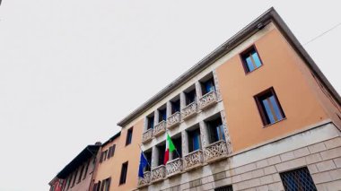 Slow motion footage of the Italian flag and the EU European flag blowing in the wind on the side of a building in the town of Verona in Italy