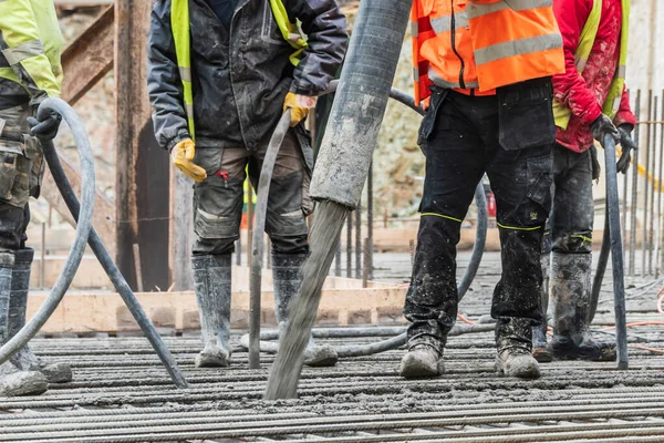 Beton döküm çalışmaları sırasında beton vibratörle katı tutarlılığı sıkıştıran bir grup inşaat işçisi..