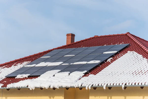 Evin çatısı karla kaplı, kışın güneş panelleri. Güneşten gelen elektrik - kış boyunca karın altında fotovoltaik güneş panelleri. Güneşli bir gün, mavi gökyüzü ve telif alanı.