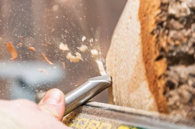 Torna tezgahında ahşap kaseler yapmak. Torna makinesinin yakın çekim görüntüsü. Elinde keski ve talaş olan bir adam uçuyor..