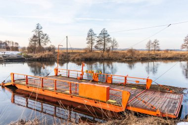 İki kıyıya da kabloyla bağlı bir kablo feribotu ya da büyük bir su kütlesi. Turuncu zincir feribot, mavi su ve gökyüzü.