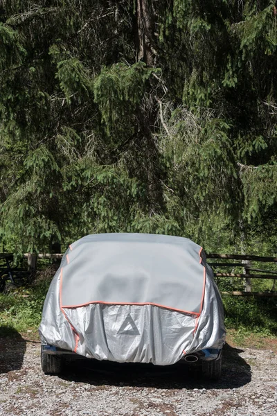 The gray and silver sun protection car cover. Car parked in the forest parking lot covered with a cover to protect against sun and dust