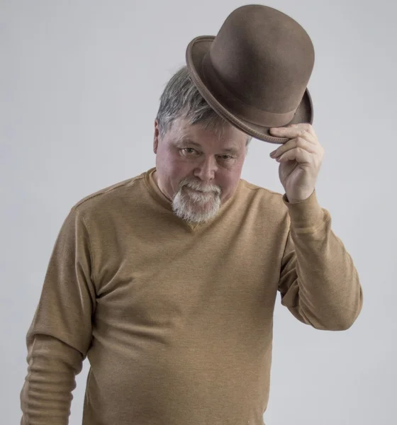 Homem mais velho em camisola marrom doffing marrom derby e sorrindo — Fotografia de Stock