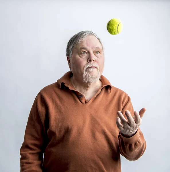 Älterer bärtiger Mann in orangefarbenem Pullover wirft grünen Tennisball — Stockfoto