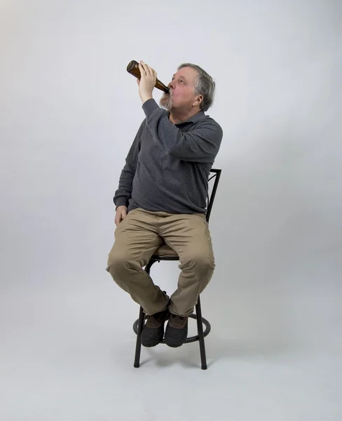 Older man sitting on stool drinking beer from bottle Stock Picture