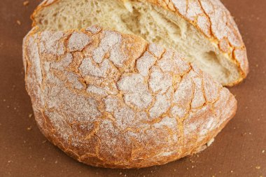 Kahverengi arka planda iki parçaya bölünmüş yuvarlak beyaz ekmek var..