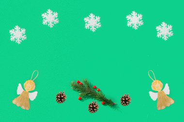 Kar taneleri, çam kozalakları, köknar dalları, yeşil arka plandaki melekler. Metin için bir yer var.