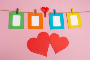 Renkli fotoğraf çerçeveleri ipe mandallarla tutturulmuş. Kırmızı kalplerle süslenmiş pembe arka plan. Sevgililer Günü.