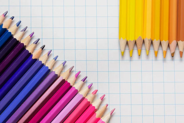 On a white checkered background there are yellow, red, blue, brown pencils.